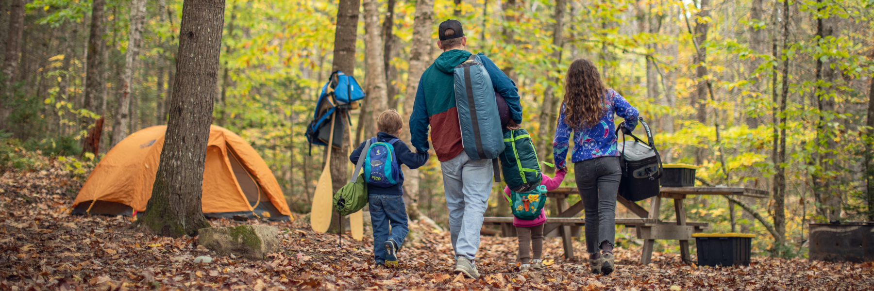 Two adults and a child near a tent in trees.