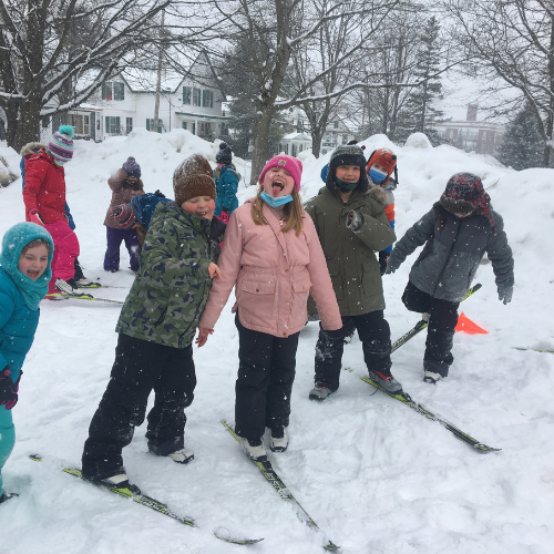Children enjoying skiing in the snow, wearing colorful winter clothing and laughing together. Snowy landscape in the background.