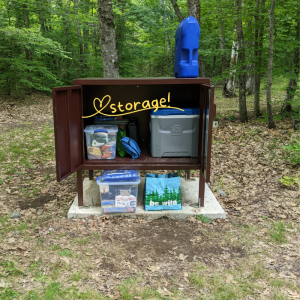 Groceries stacked inside a brown metal storage box at a campsite.