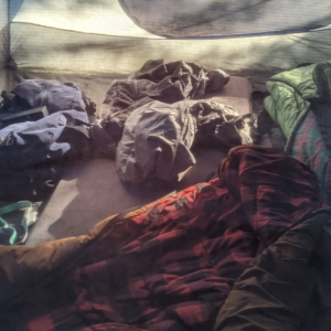 The interior of a tent with rumpled blankets and clothes.