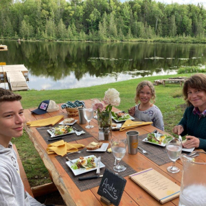 Three people eating dinner at a picnic table in front of a pond.