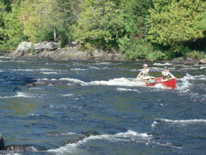 Two people in a red canoe paddling in a fast-moving river.