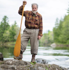 A man standing with a canoe paddle next to a river.