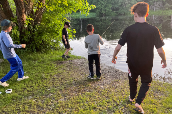 Four boys gathered on a riverbank. One is fishing.