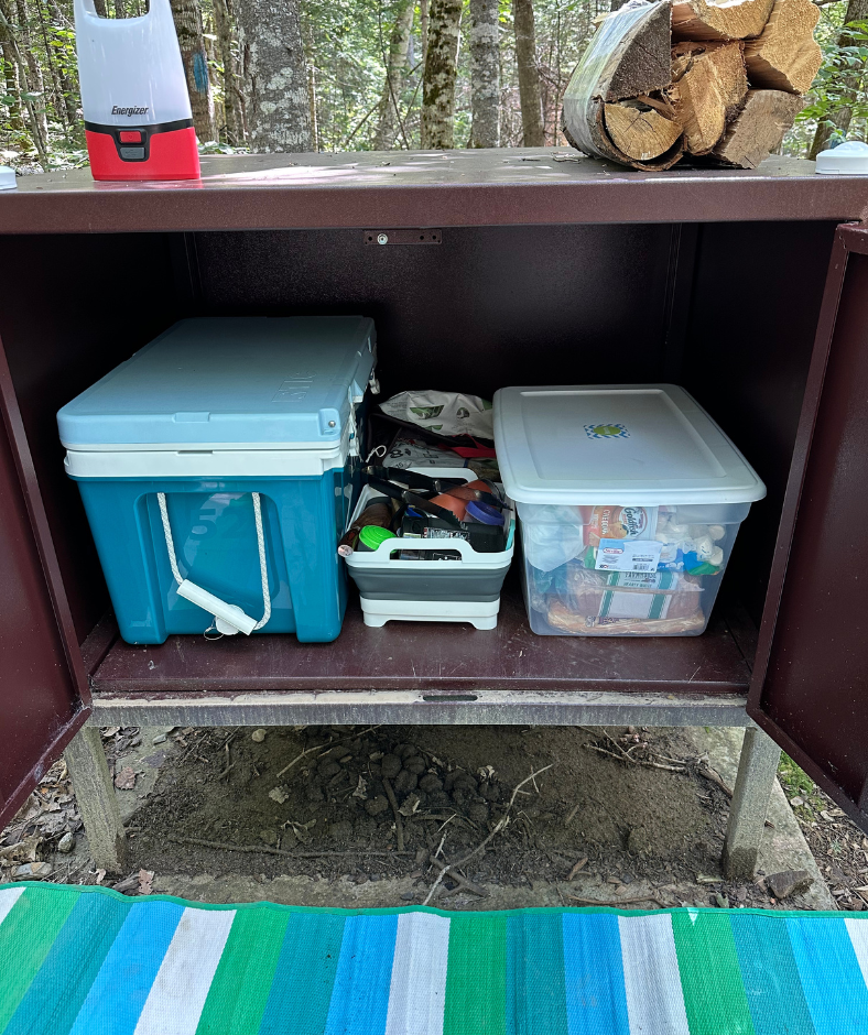 A brown metal locker box on legs with coolers and food inside.