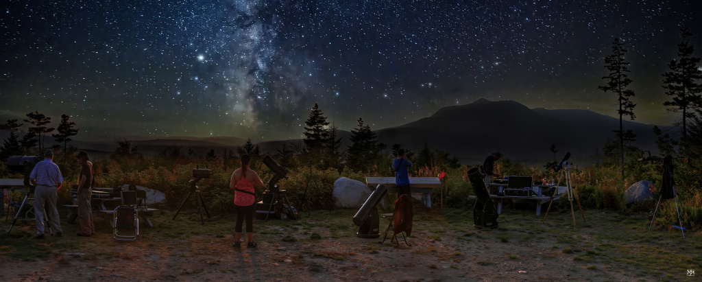 A view of the Milky Way above a mountain. People in the foreground are looking at telescopes.