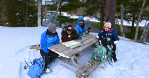 Four people seated at a picnic table in the snow.