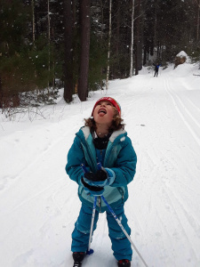 A young girl on cross country skis looks at the sky.