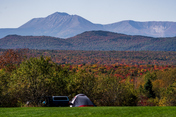 A scenic view of colorful trees in autumn with a tent and mountains in the background under clear blue skies.