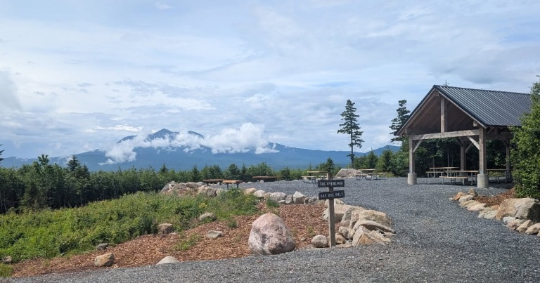 View of a mountain backdrop with a shelter, picnic tables, and trails, surrounded by greenery and boulders.