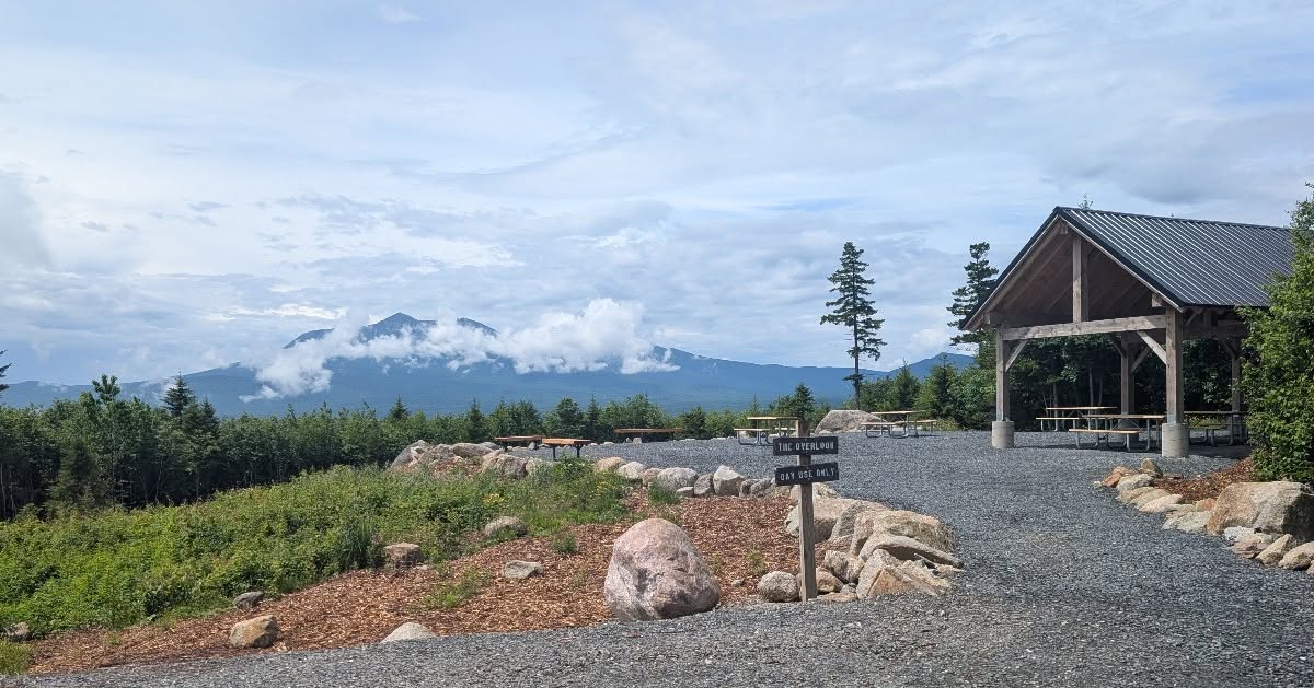 View of a mountain backdrop with a shelter, picnic tables, and trails, surrounded by greenery and boulders.
