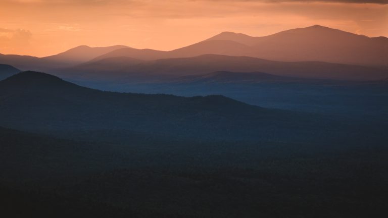 Photo of the sunsetting over layers of dark mountains in the foreground