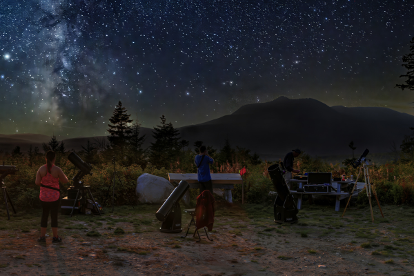 People gathered with telescopes at night with the Milky Way.