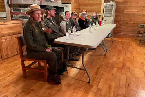 Rangers and other outdoor professionals in uniform are seated at a table facing an audience (not shown).