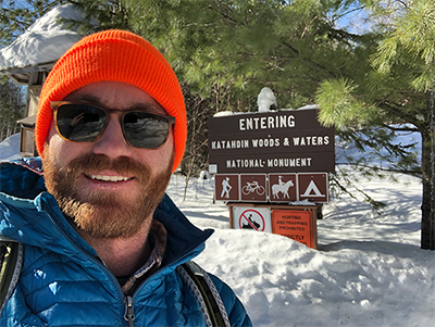 Brian Hinrichs by the sign at the north entrance of Katahdin Woods and Waters National Monument