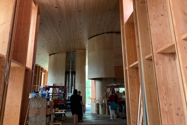 Three people facing away from the camera, assembled inside a large, wood, partially completed building.