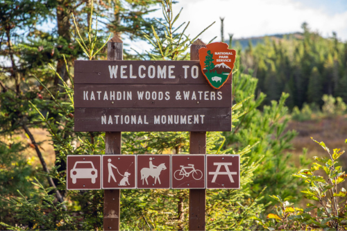 A wooden sign for Katahdin Woods and Waters National Monument with the NPS arrowhead logo.